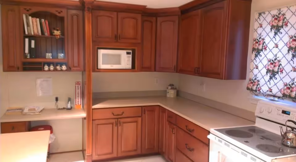 Kitchen with wooden cabinets, a microwave, electric stove, L-shaped countertop and a floral curtain over the window.