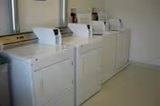 Four white laundry machines lined up against the wall in a bright, clean laundry room.