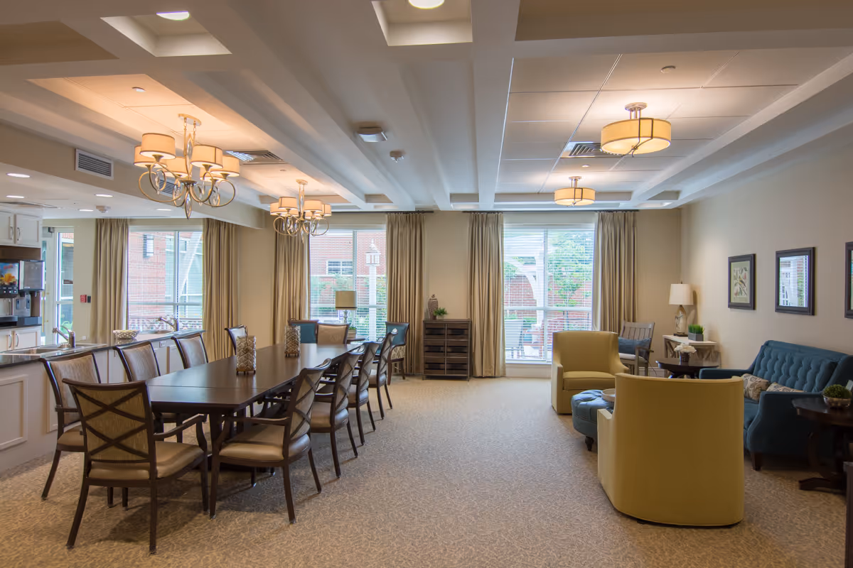 Spacious communal dining and lounge area with a long dining table, chairs, and seating near large windows.