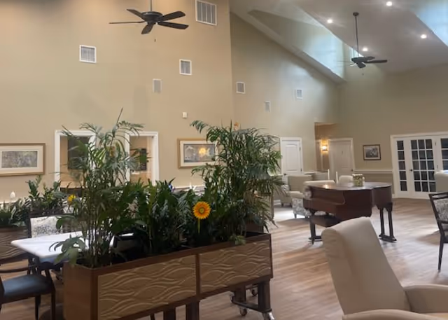Senior living facility lounge interior with plants, seating, and a piano.