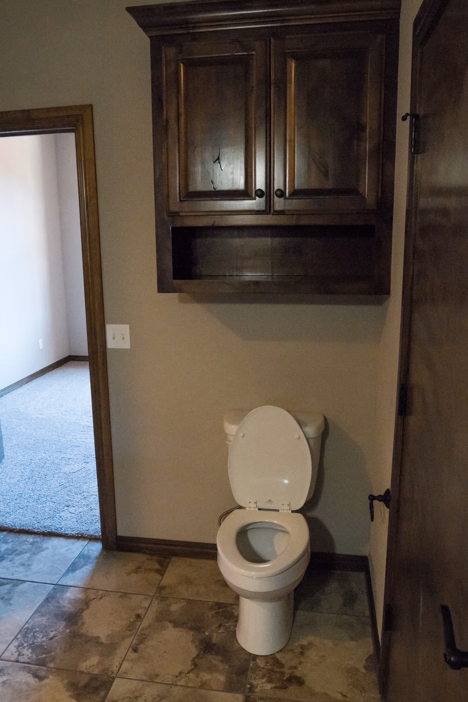 Toilet with open lid beneath a wooden wall cabinet in a bathroom with tiled floor.