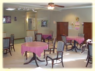 Dining room with several round tables covered in pink tablecloths and wooden chairs under a ceiling fan.