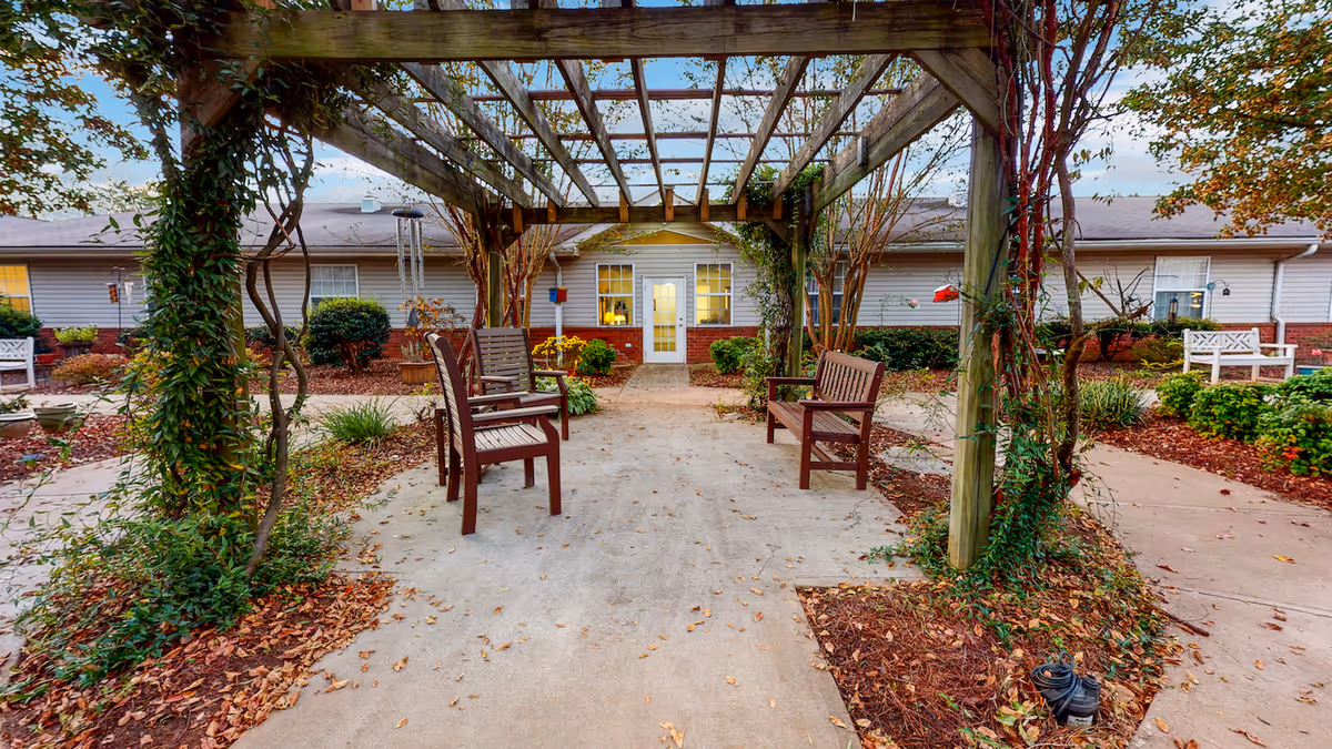 Courtyard with a wooden pergola, benches, walkways, and landscaping in front of a single-story building.