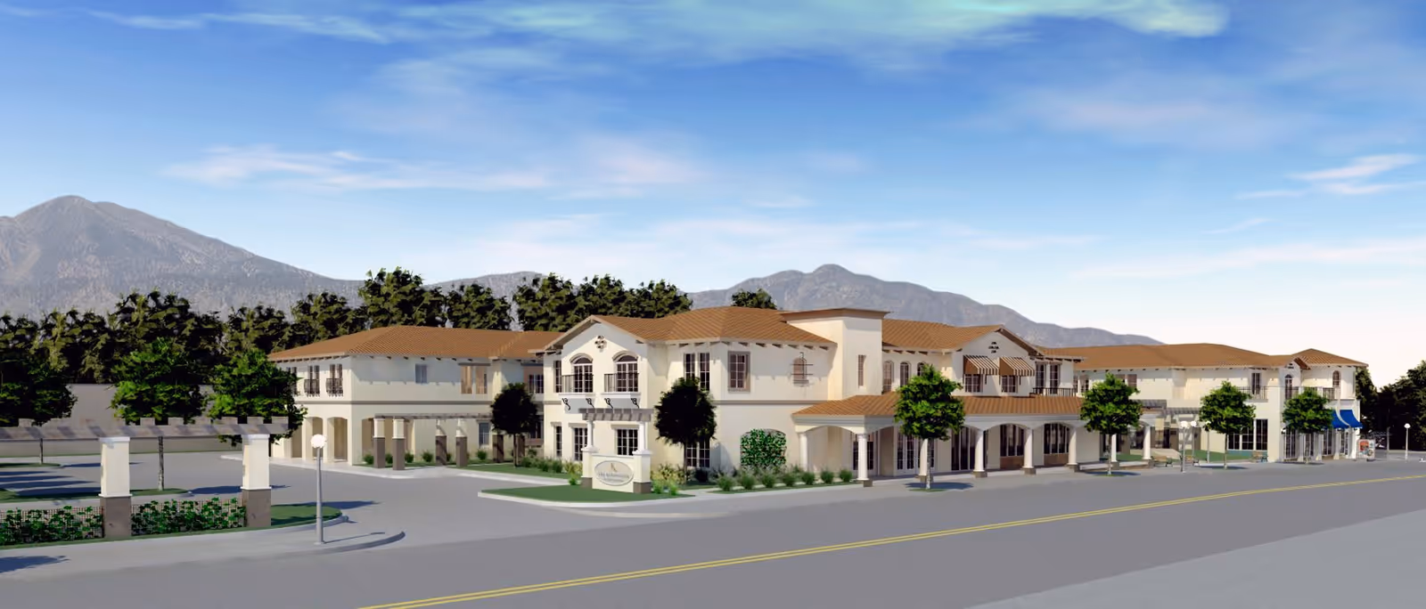 Exterior view of a large, two-story senior living facility building with beige walls and brown tiled roofs, surrounded by trees and landscaping, with mountains in the background under a blue sky.