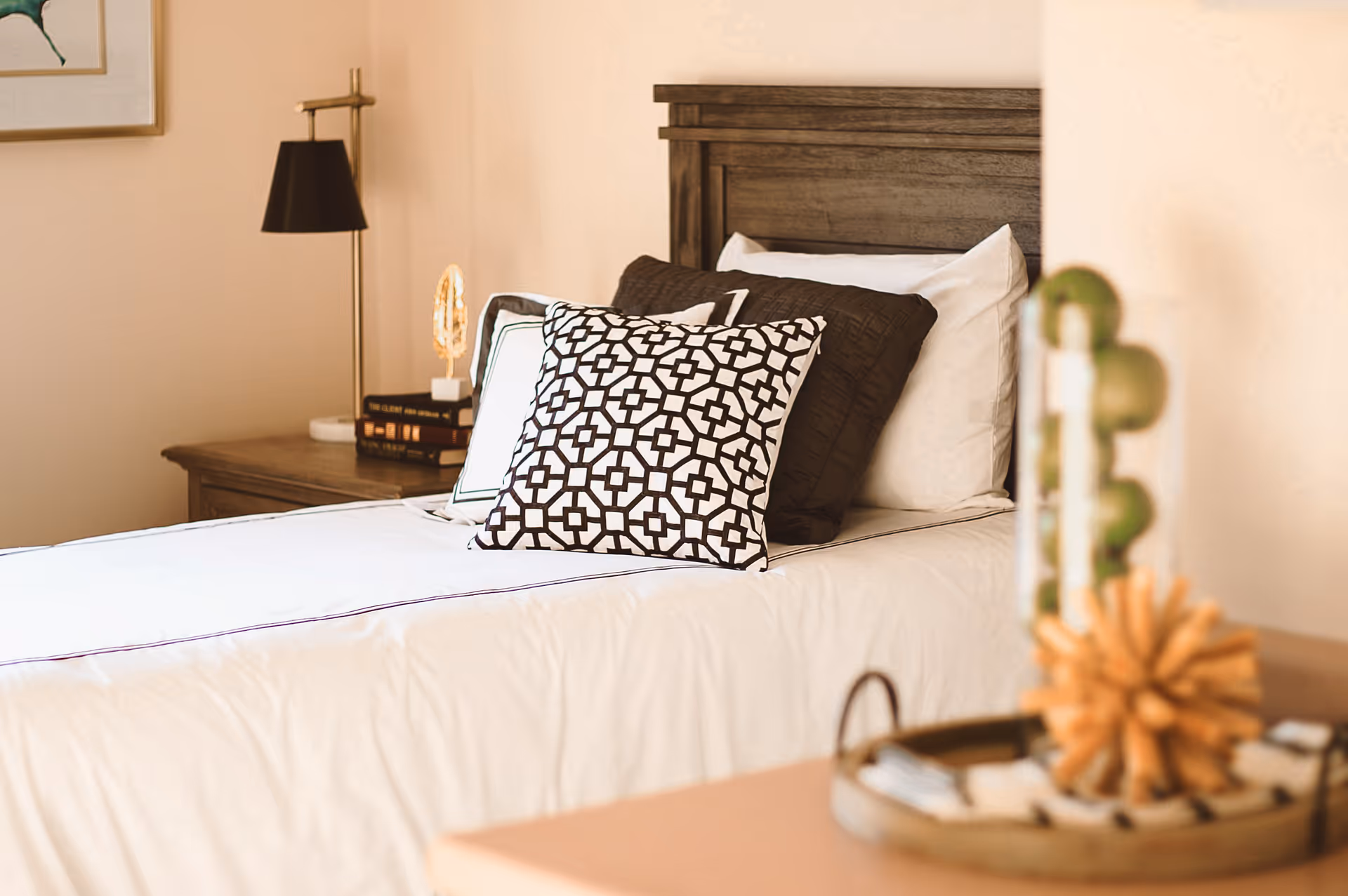 A neatly made bed with patterned pillows and a wooden headboard beside a nightstand with a lamp.