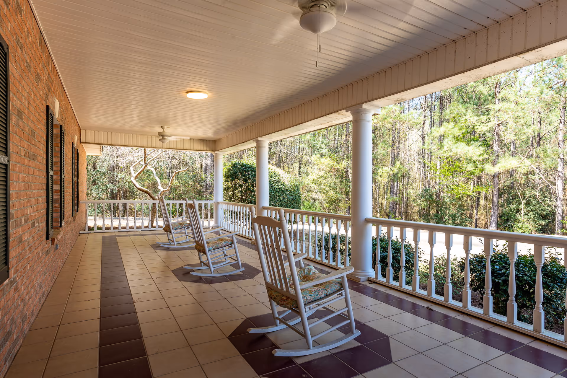 Covered front porch with white rocking chairs overlooking a wooded yard.