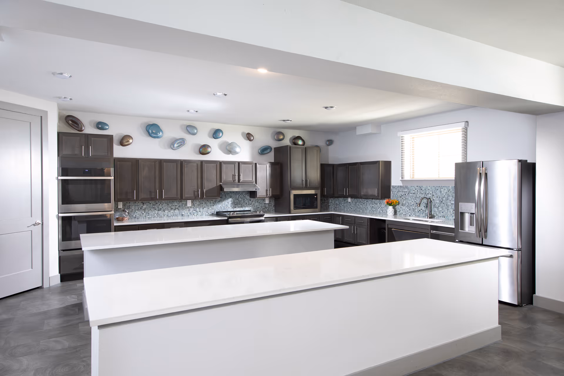 Modern open kitchen with two large white islands, dark wood cabinets, stainless steel appliances and decorative wall art above the backsplash.
