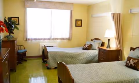 Two twin beds with matching bedding, nightstands, lamps, and a window in a yellow-walled bedroom.