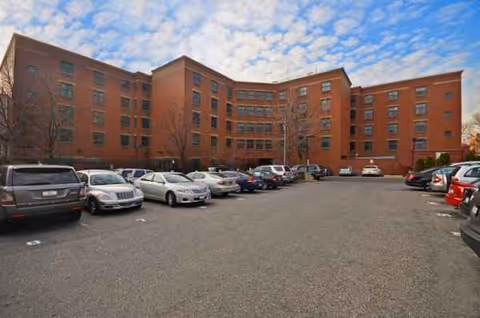A brick senior living facility with several parked cars in front.