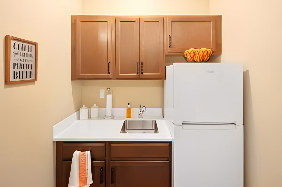 Small kitchenette with a white countertop and sink, brown cabinets, and a white refrigerator.