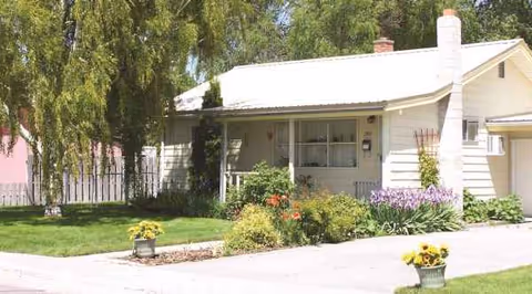 A single-story white building with a garden, flowers, and a driveway in front.