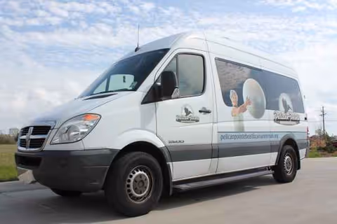 A white Pelican Pointe transportation van is parked on a driveway with branding.