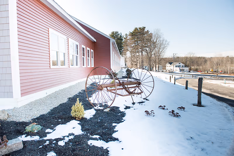 Exterior view of Carriage Hill Assisted Living with red siding, snow, and wagon wheel sculpture.