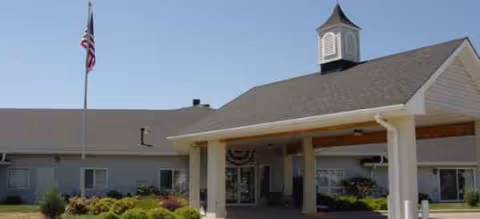 Front exterior of Kinship Pointe at Wayne with flagpole, clock tower, and covered entrance.