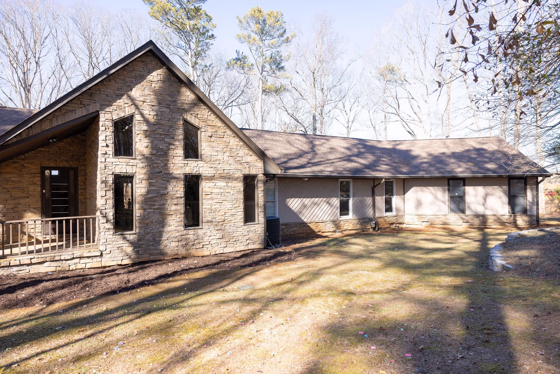 Single-story stone-and-siding building with tall windows and a grassy yard under bare trees.