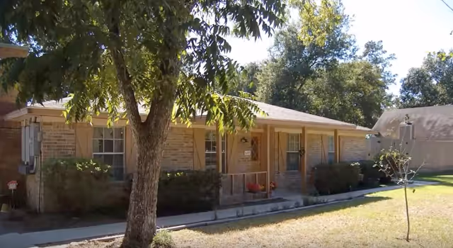 One-story brick senior living facility with a front porch, trees, and a grassy lawn.
