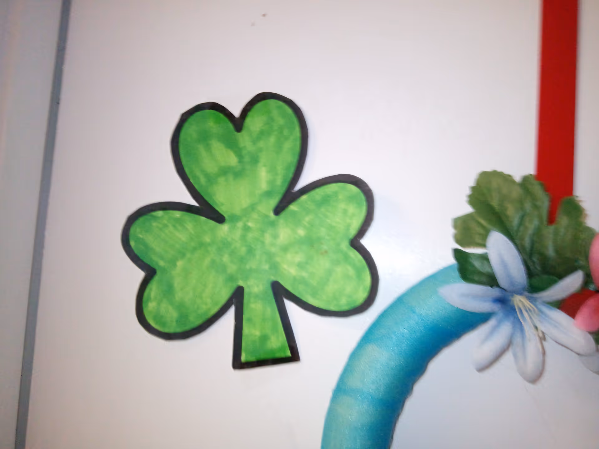 Green paper shamrock decoration and part of a floral wreath on a white door.
