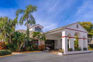 The entrance of Regency Residence featuring a covered portico, palm trees, and vibrant landscaping.