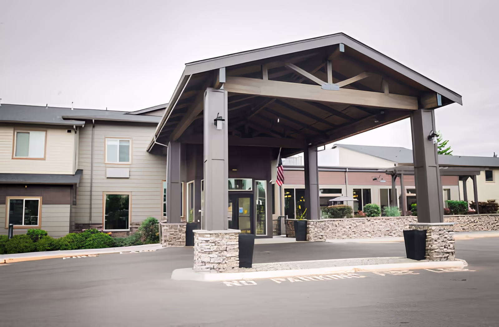 Entrance of Village Concepts of Burien - El Dorado West facility showing a covered driveway with stone pillars and a building with multiple windows in the background.