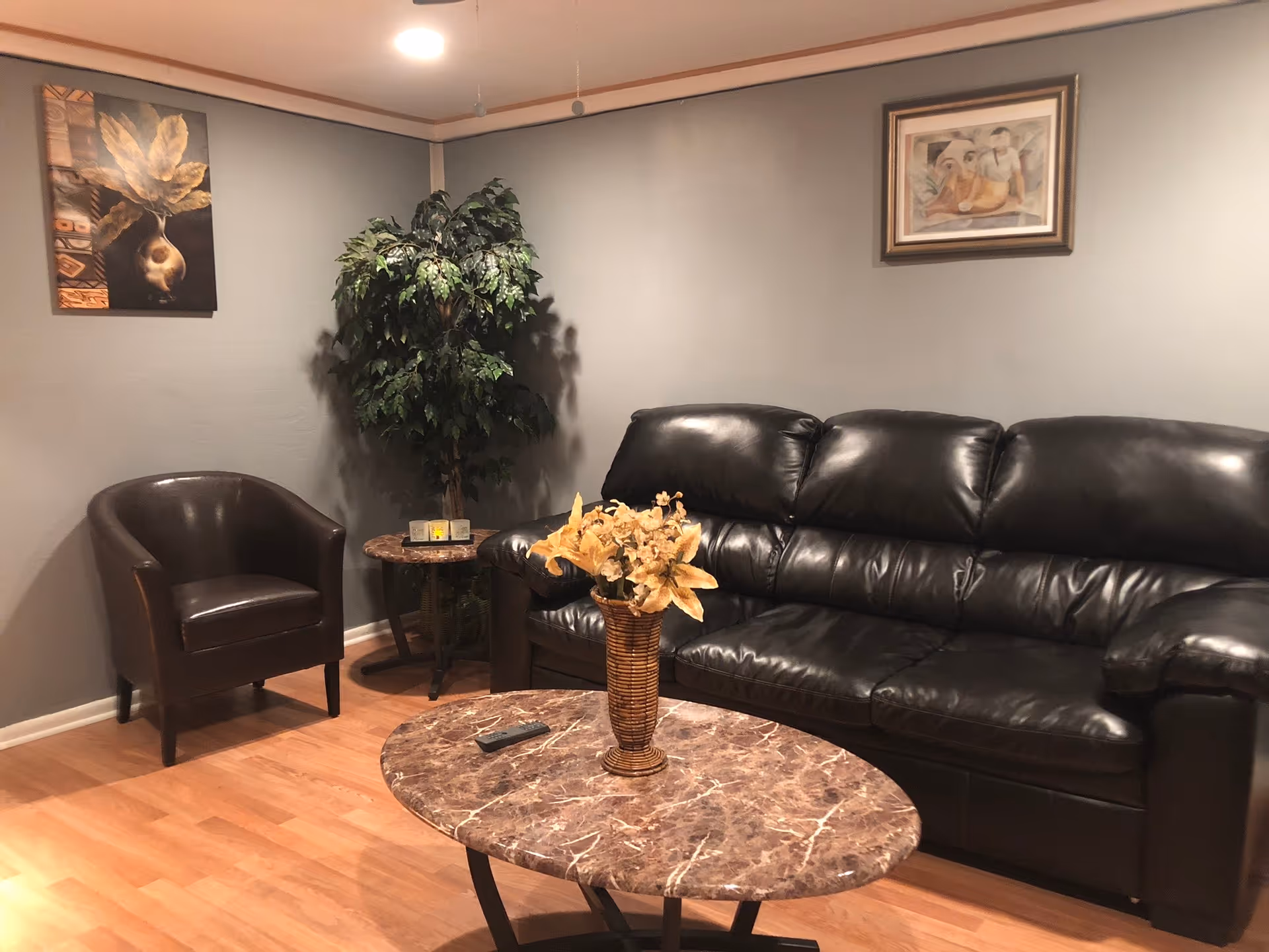 A cozy living room lounge with a black leather sofa, chair, plant, and marble coffee table.