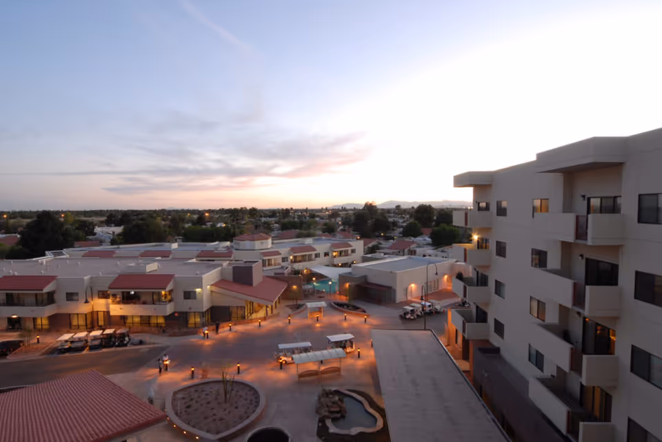 Evening aerial view of a senior living campus with multi-story buildings, courtyards, and lit walkways.
