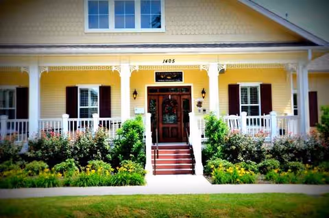 Yellow front porch villa with white railing, steps, and manicured garden.