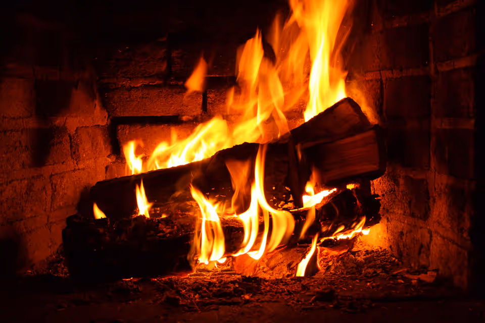 A close-up view of a burning fireplace with logs engulfed in bright orange flames inside a brick hearth.
