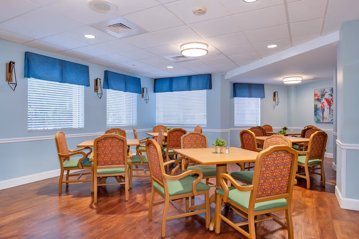 Bright communal dining room with wooden tables and patterned chairs in a senior living facility.