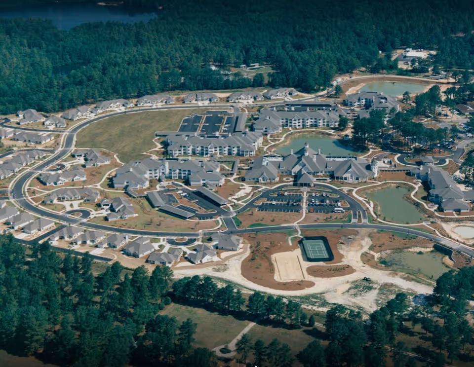 Aerial view of Belle Meade Retirement Community showing multiple buildings, parking lots, walking paths, ponds, and surrounding wooded areas.