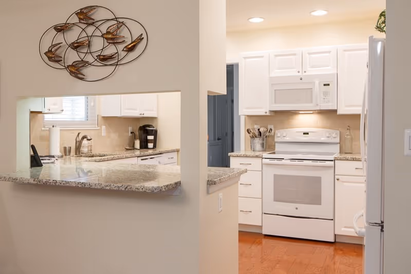 Bright modern kitchen with white cabinets, a white stove and microwave, granite countertops, and a pass-through counter opening.