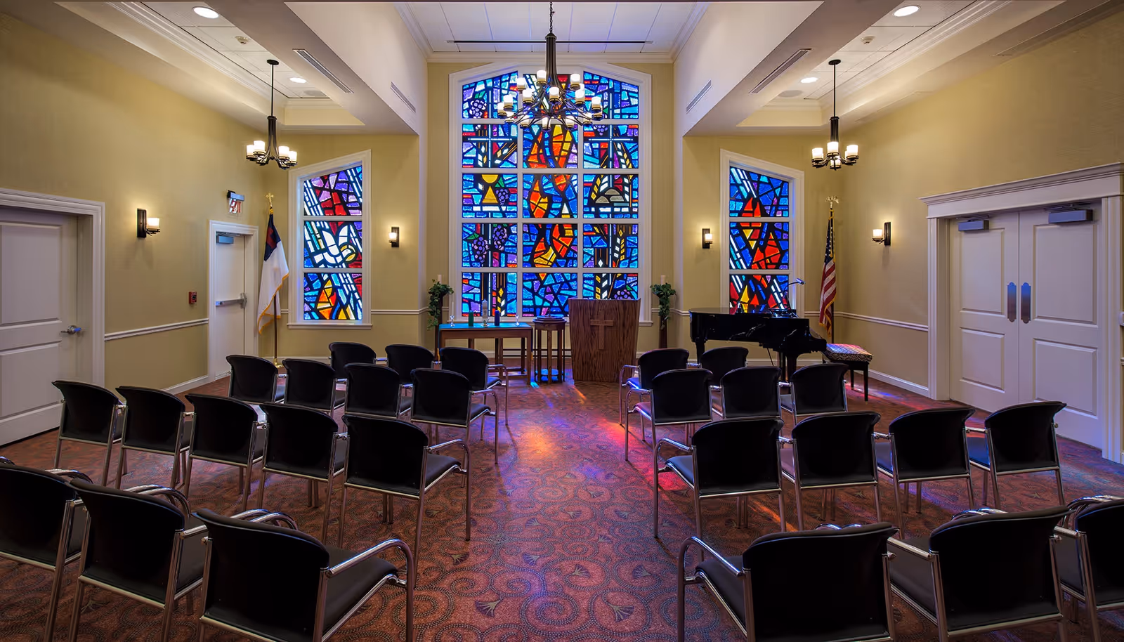 Interior chapel-style meeting room with rows of chairs facing a pulpit and large colorful stained glass windows.