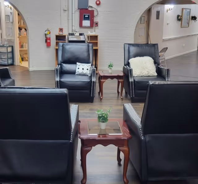 A communal seating area with black leather armchairs arranged around wooden side tables topped with small potted plants.