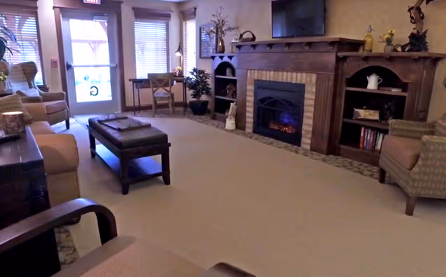 A cozy sitting room with upholstered chairs, an ottoman, a fireplace with mantel and TV, and a glass entry door with windows.