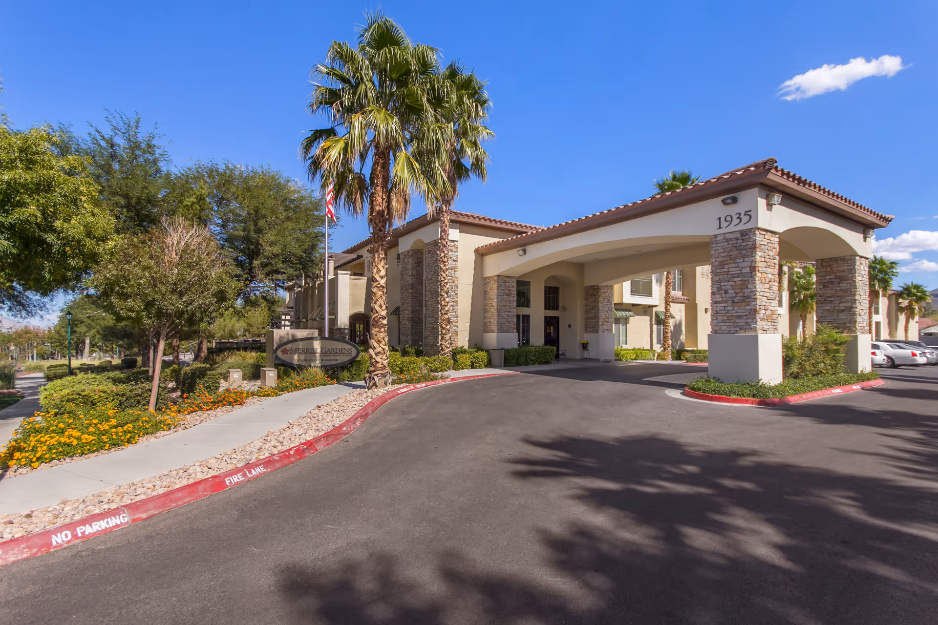 Front entrance and porte-cochere of Merrill Gardens at Green Valley Ranch with palm trees and landscaped driveway.