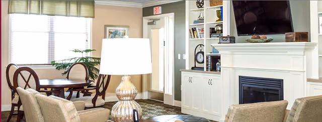 Cozy living room in a senior facility with fireplace, TV, built-ins, and seating.