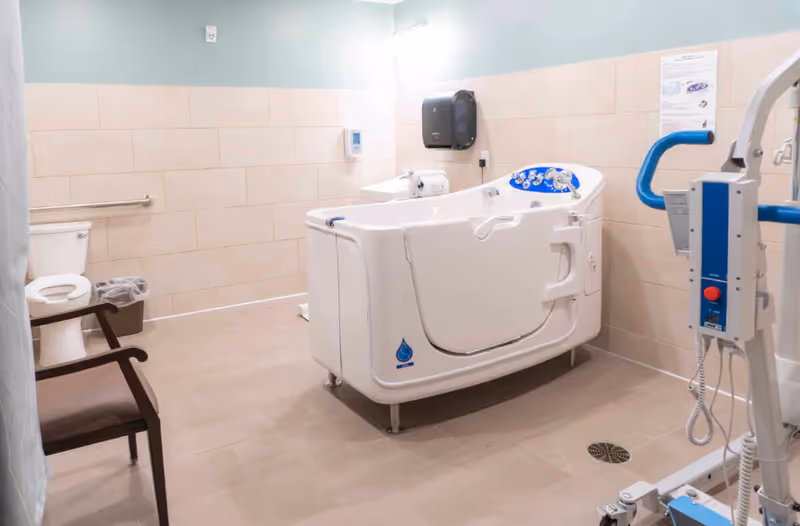 Accessible bathroom with a walk-in bathtub, patient lift, toilet, sink and chair.