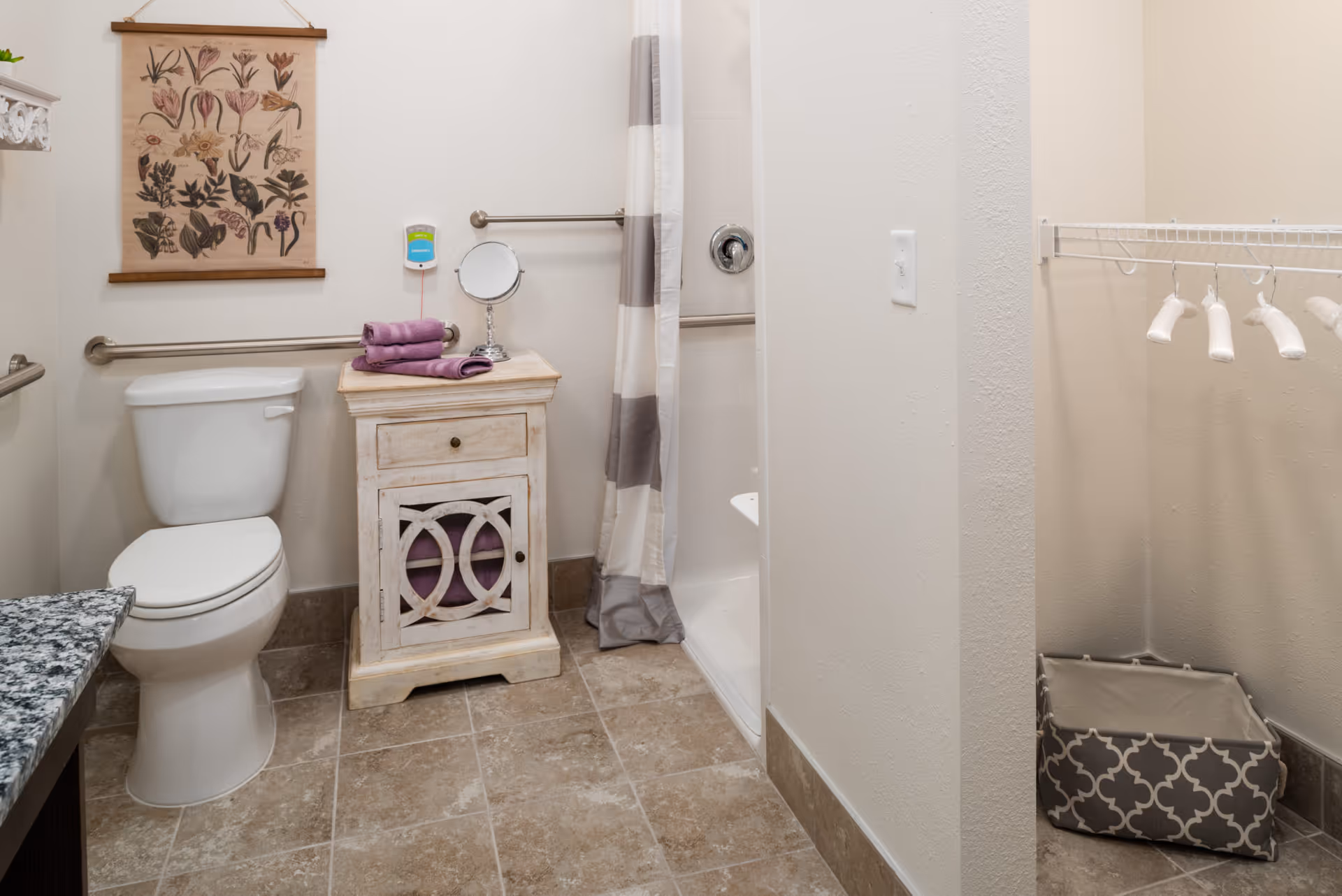 Bathroom featuring a toilet, a small distressed cabinet topped with purple towels and a mirror, a curtained shower with grab bars, and an adjacent open closet area.