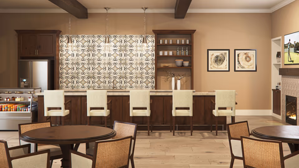 Interior view of a dining area with a long counter and five high chairs. Behind the counter are wooden cabinets, shelves with cups and bowls, and a patterned tile backsplash. In the foreground are round tables with chairs. To the right, there is a fireplace with a TV mounted above it showing a golf scene. The room has wooden beams on the ceiling and light-colored walls.