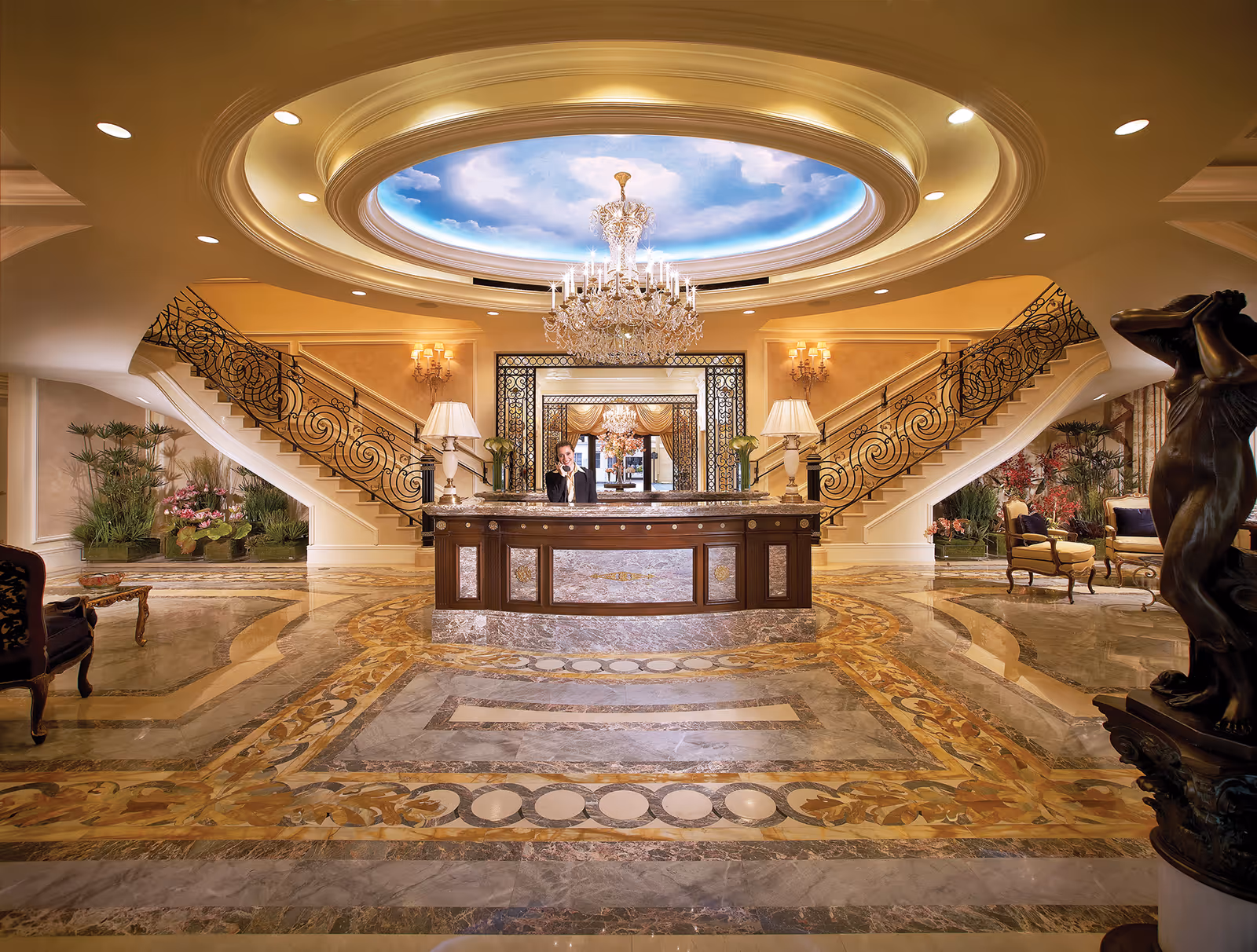 Opulent interior lobby with a central reception desk, twin curved staircases, crystal chandelier and painted domed ceiling.