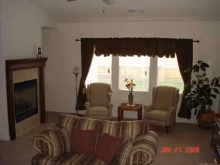 Living room seating area with a fireplace, sofa, and two beige armchairs near a curtained window.