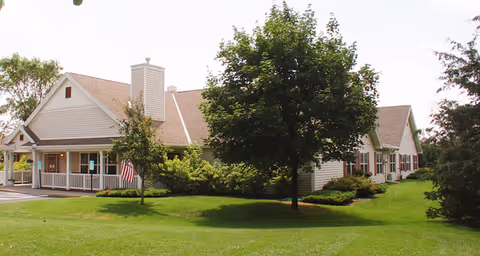 Single-story senior living facility building with a covered entrance, green lawn and trees.