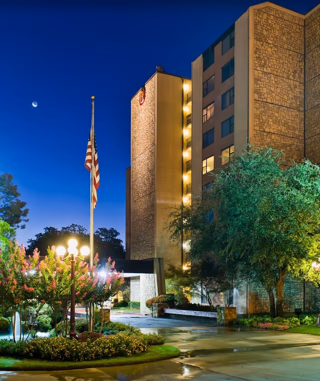 Night view of the senior living facility's landscaped entrance with an American flagpole and a multi-story stone-clad building lit up.