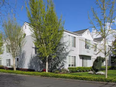 Two-story white senior living building with trees and a manicured lawn.