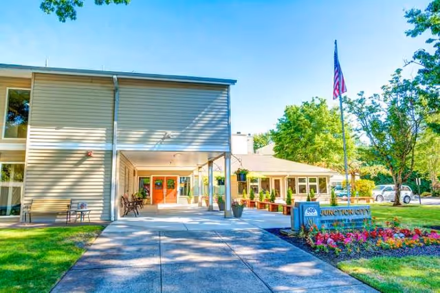 Front exterior of Junction City Retirement and Assisted Living with walkway, benches, and landscaping.