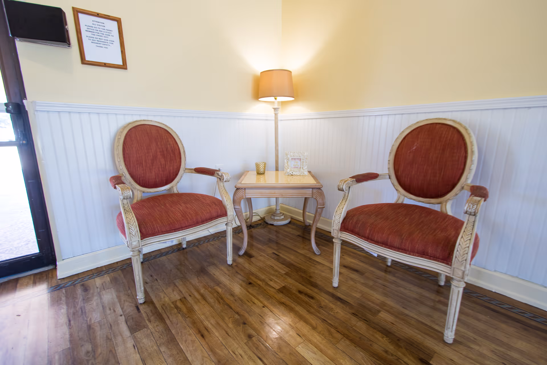 Two upholstered red armchairs flanking a small side table with a lamp against a wainscoted wall.