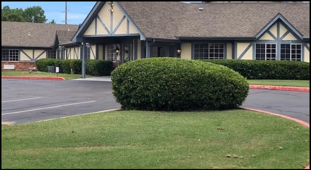 Exterior view of The Cottage At Woodland Hills building with hedges and parking.