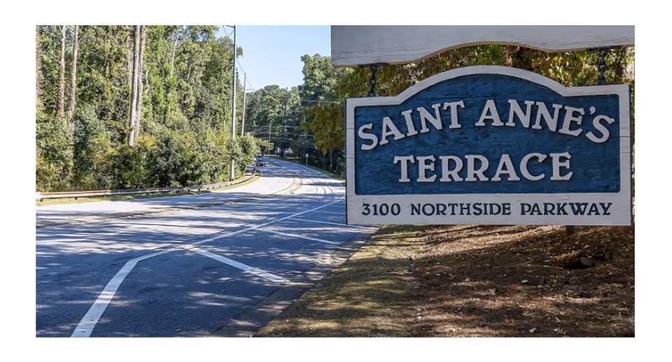 Wooden entrance sign reading "Saint Anne's Terrace 3100 Northside Parkway" beside a tree-lined road.