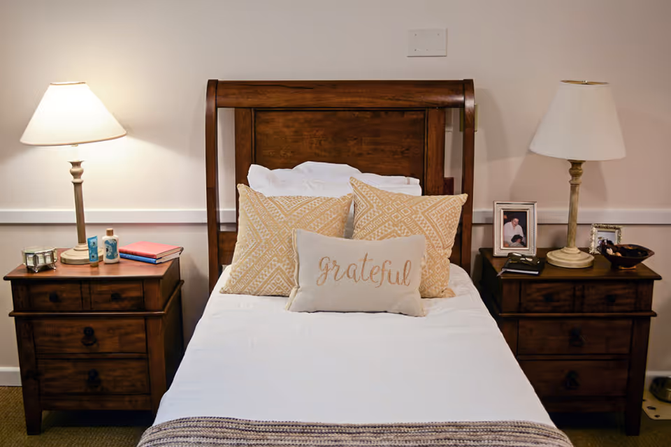 A neatly made single bed with a wooden headboard and a "grateful" decorative pillow, flanked by matching nightstands and lamps.