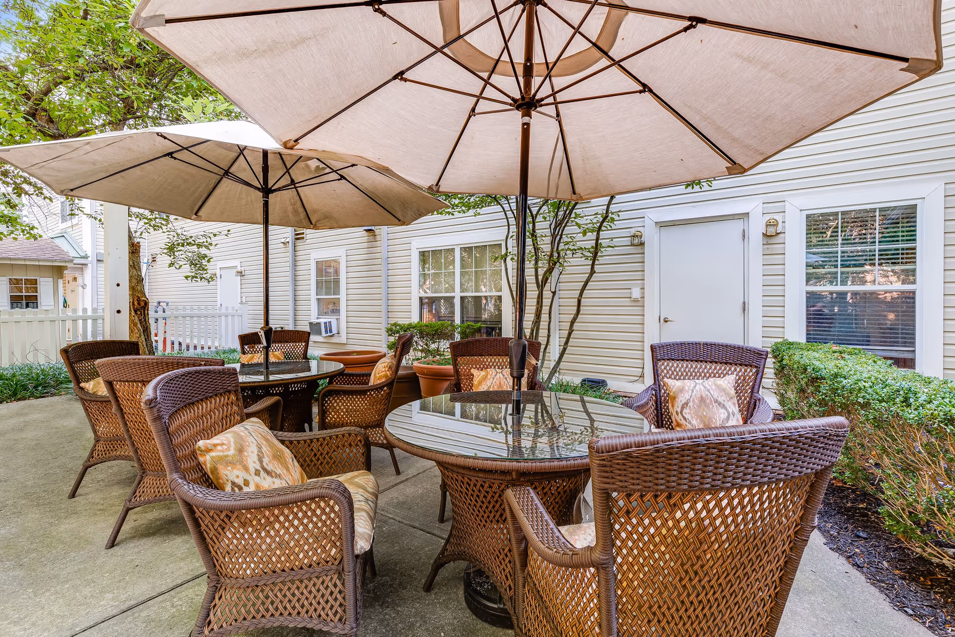 Outdoor patio area with wicker tables and chairs under large umbrellas beside a residential building.