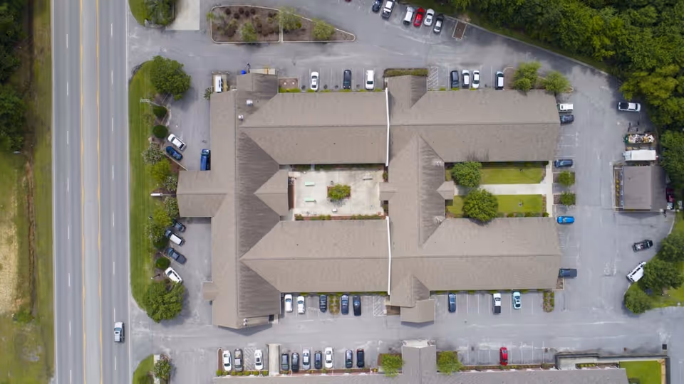 Aerial view of a U-shaped rehabilitation building with a central courtyard, surrounding parking lots, and a road alongside.